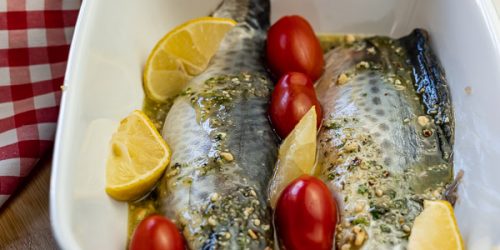 Mackerel fillet with pesto, cherry tomatoes, slices of lemon in a ceremic oven tray